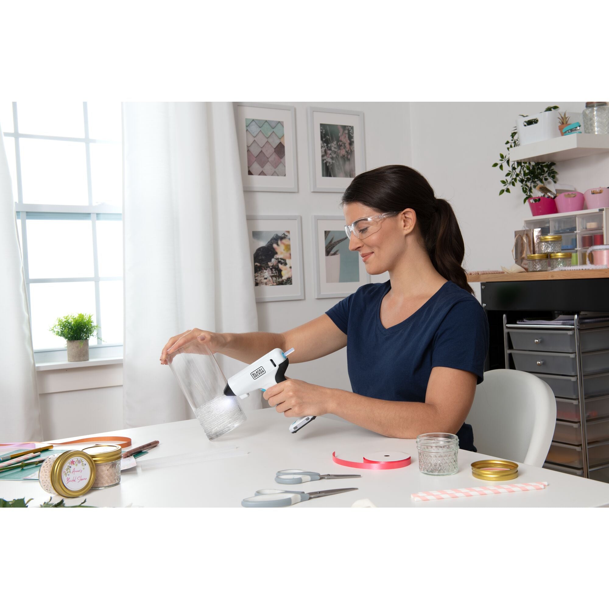 woman sitting in a craft room using a BLACK+DECKER cordless glue gun to decorate a vase and  other bridal shower decorations