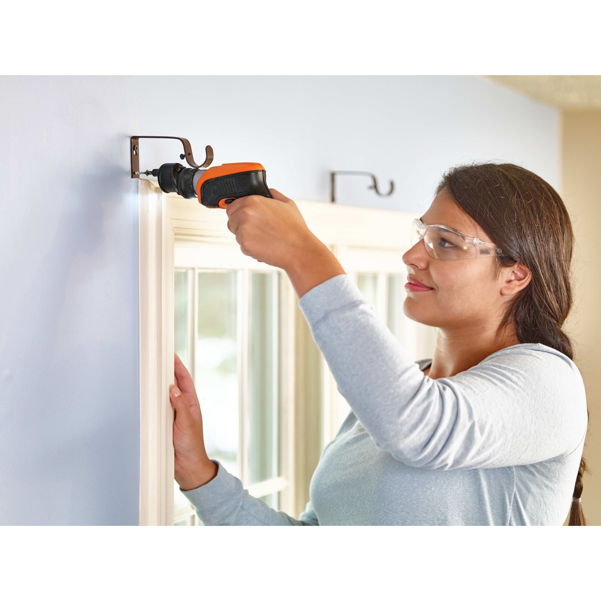 Offset attachment for 4 volt max screwdrivers attached to the screwdriver being used to drill a screw into a wall by a person.