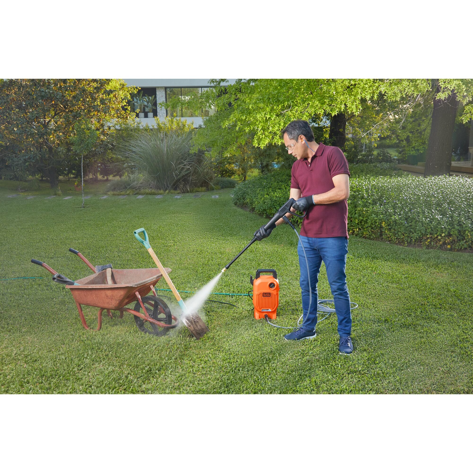 Man using BLACK+DECKER 1,700 MAX psi* pressure washer with 40\u02danozzle to clean dirt off of a shovel and wheelbarrow