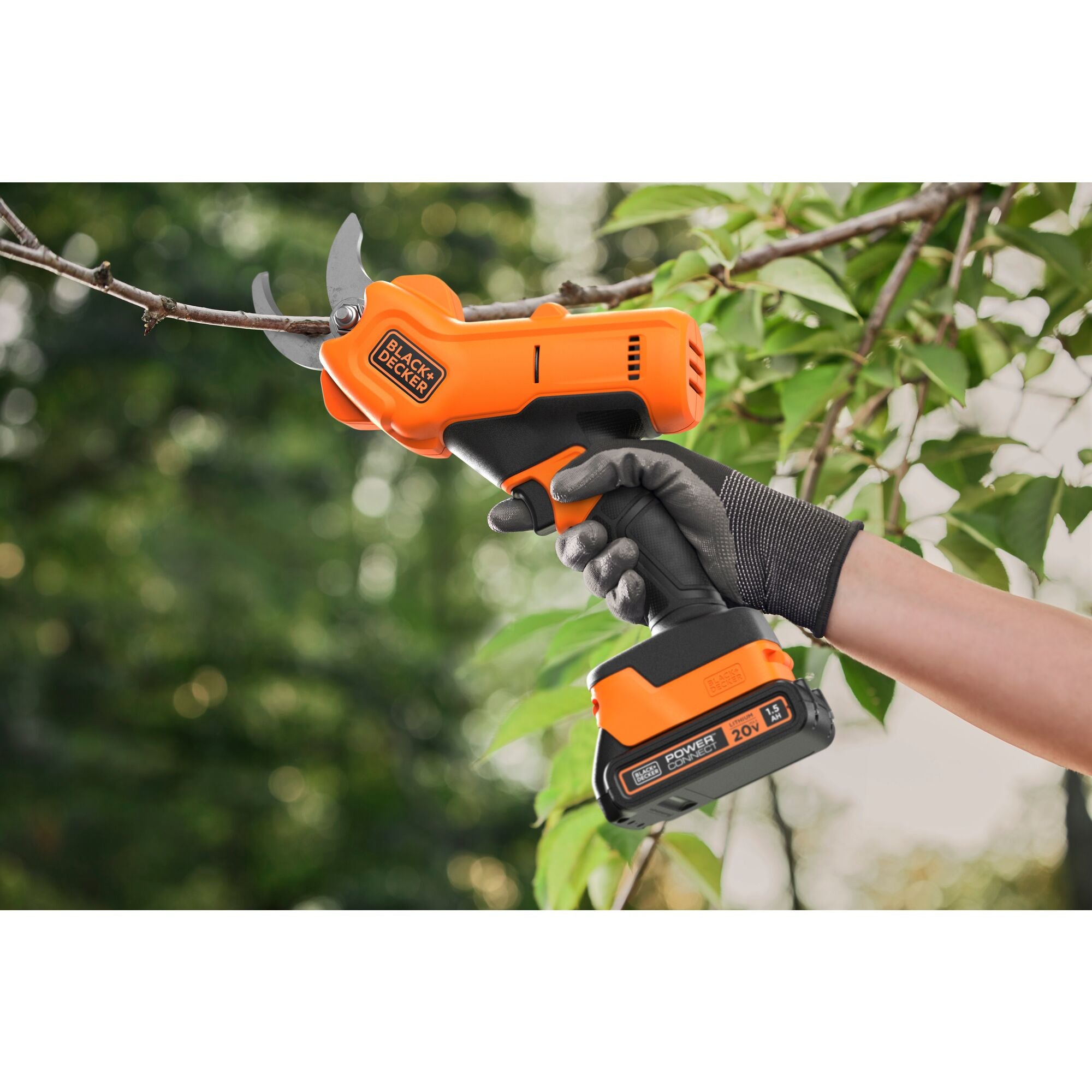 Hand with black glove using BLACK+DECKER Cordless Pruner to prune a one inch branch with leaves in the background. 