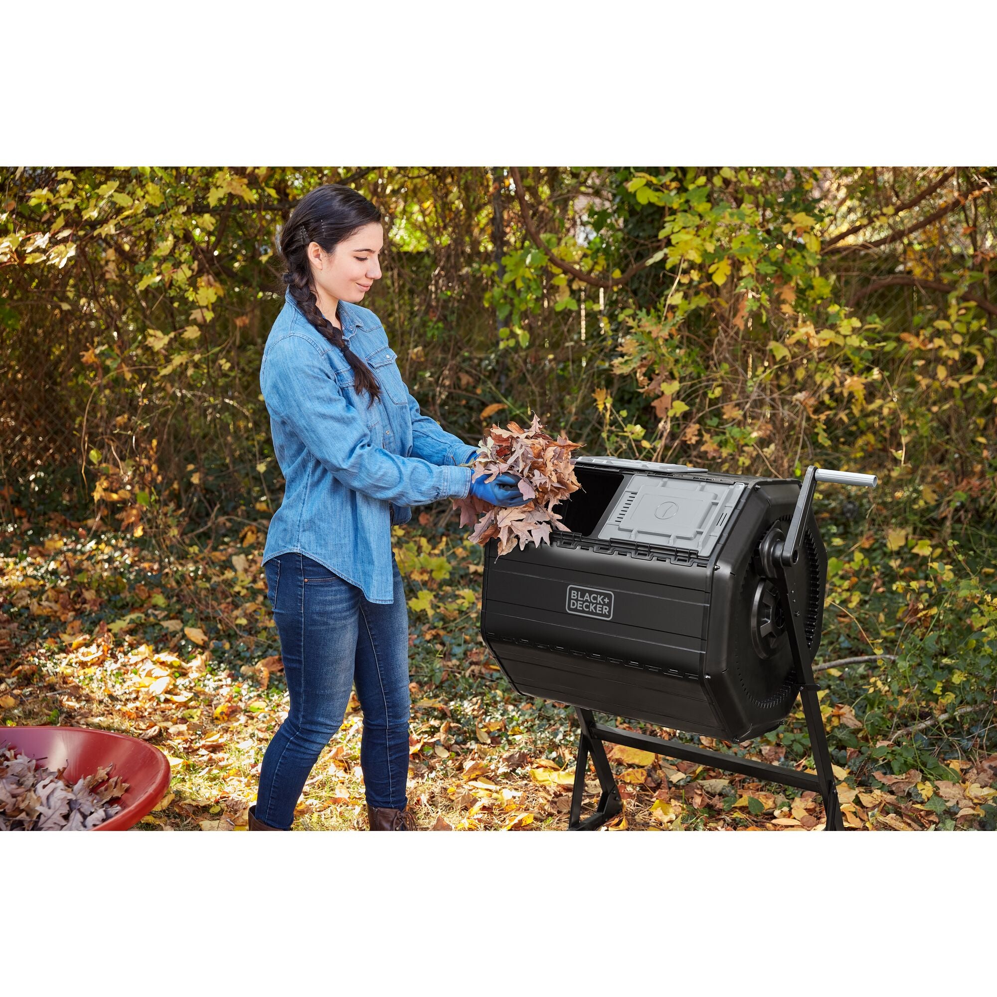 Woman putting leaves in the left chamber of the BLACK+DECKER 40 Gallon Dual Chamber Tumbler Composter