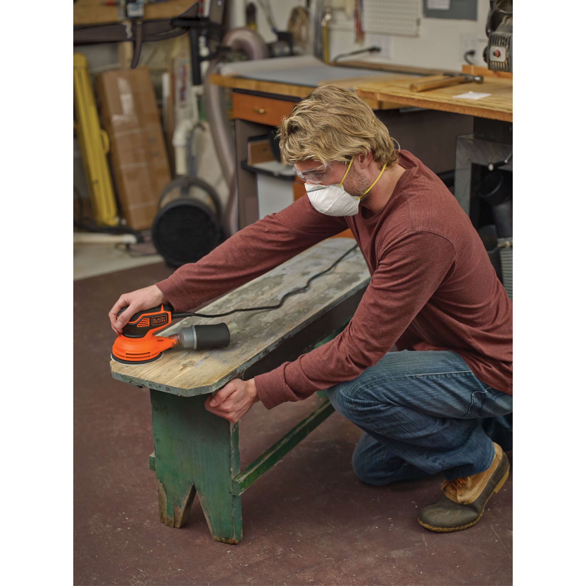 A man is using a BLACK+DECKER Electric Random Orbit Sander for sanding an old bench.