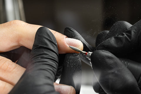 Manicurist filing a nail with gloves on using an electric file
