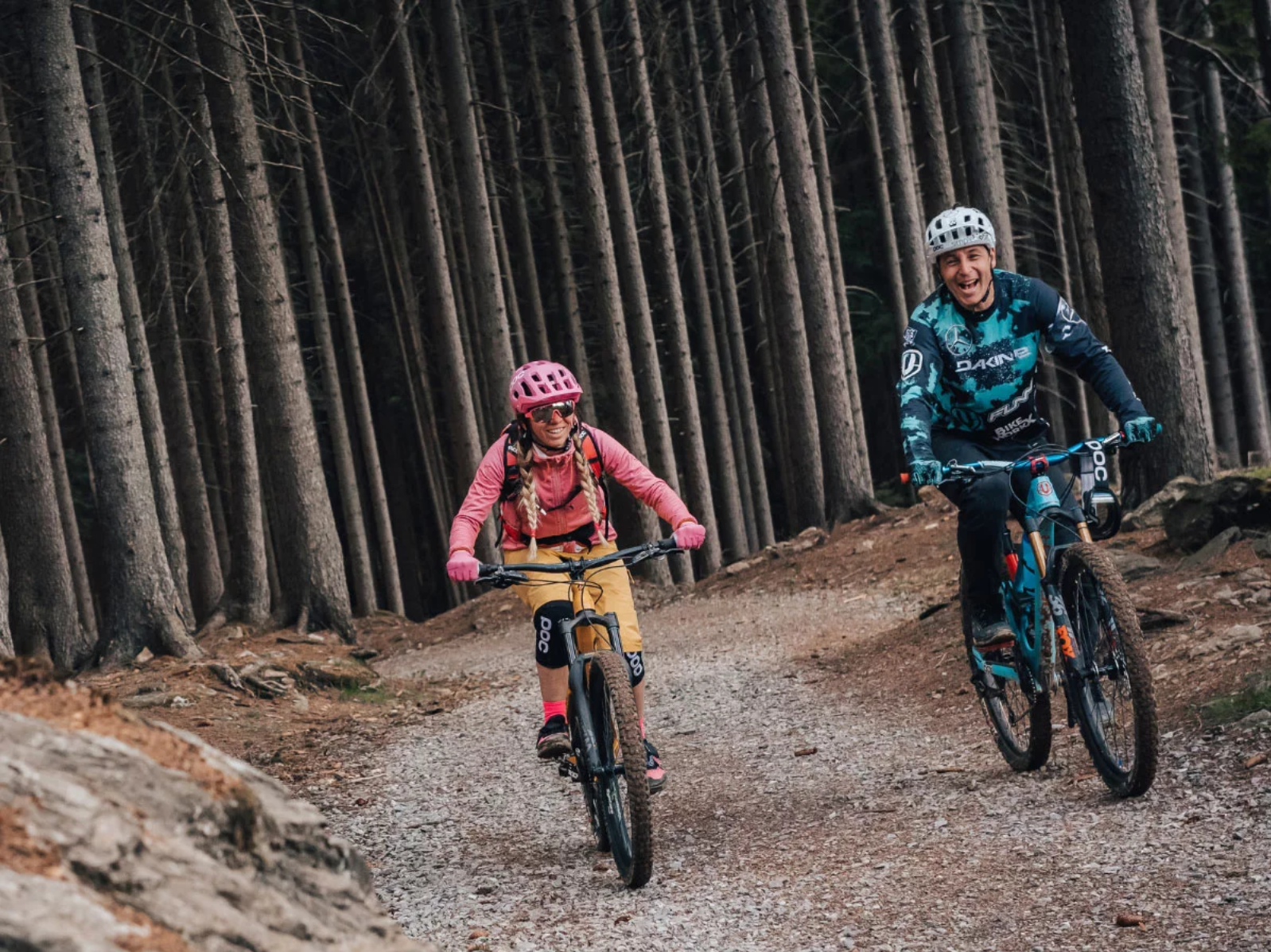 Two mountain bikers riding down a trail in the woods.