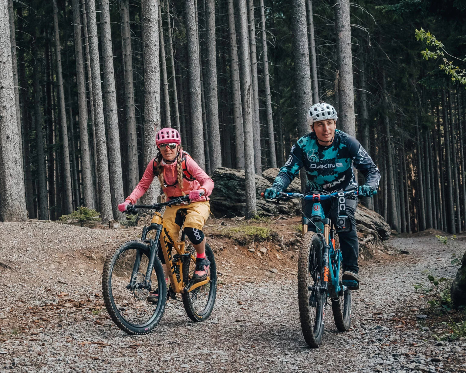 Two mountain bikers riding down a trail in the woods.