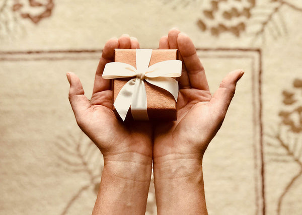 Tradition of gift giving at Christmas time. Two hands hold a small box wrapped in a bow.
