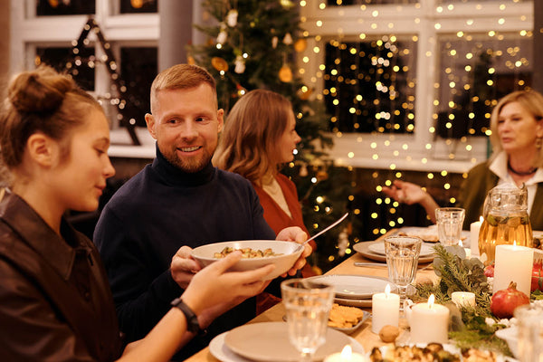 make new traditions with small Christmas gatherings. People pass food around a table with eight guests. 