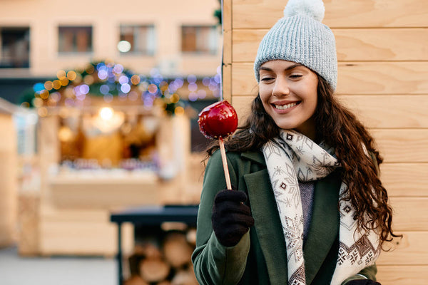Woman holds a taffy coated apple with Christmas lights in the background.