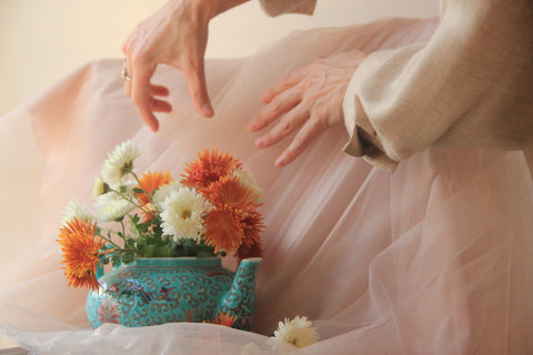 A handful of multi-colored dandelions in a pot of tea with two hands grabbing the pot