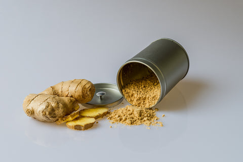 A tin jar of overflowing crushed, powdered ginger next to a ginger root