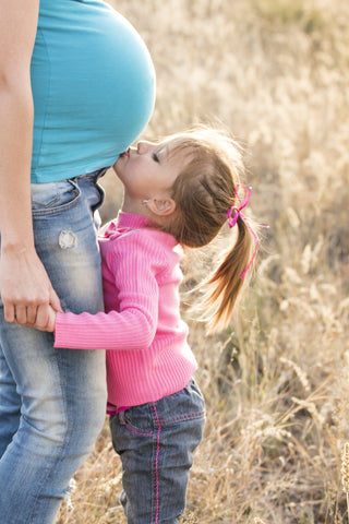 A girl kissing her mother's stomach while both stand in a field