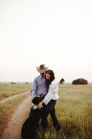 A woman and man smiling with a dog lapping into their arms