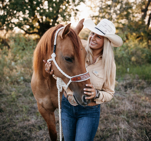 A landscape-style photo of a woman smiling and holding her horse's mane