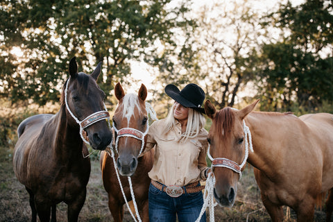 A woman smiling at the three horses she has on either side of her