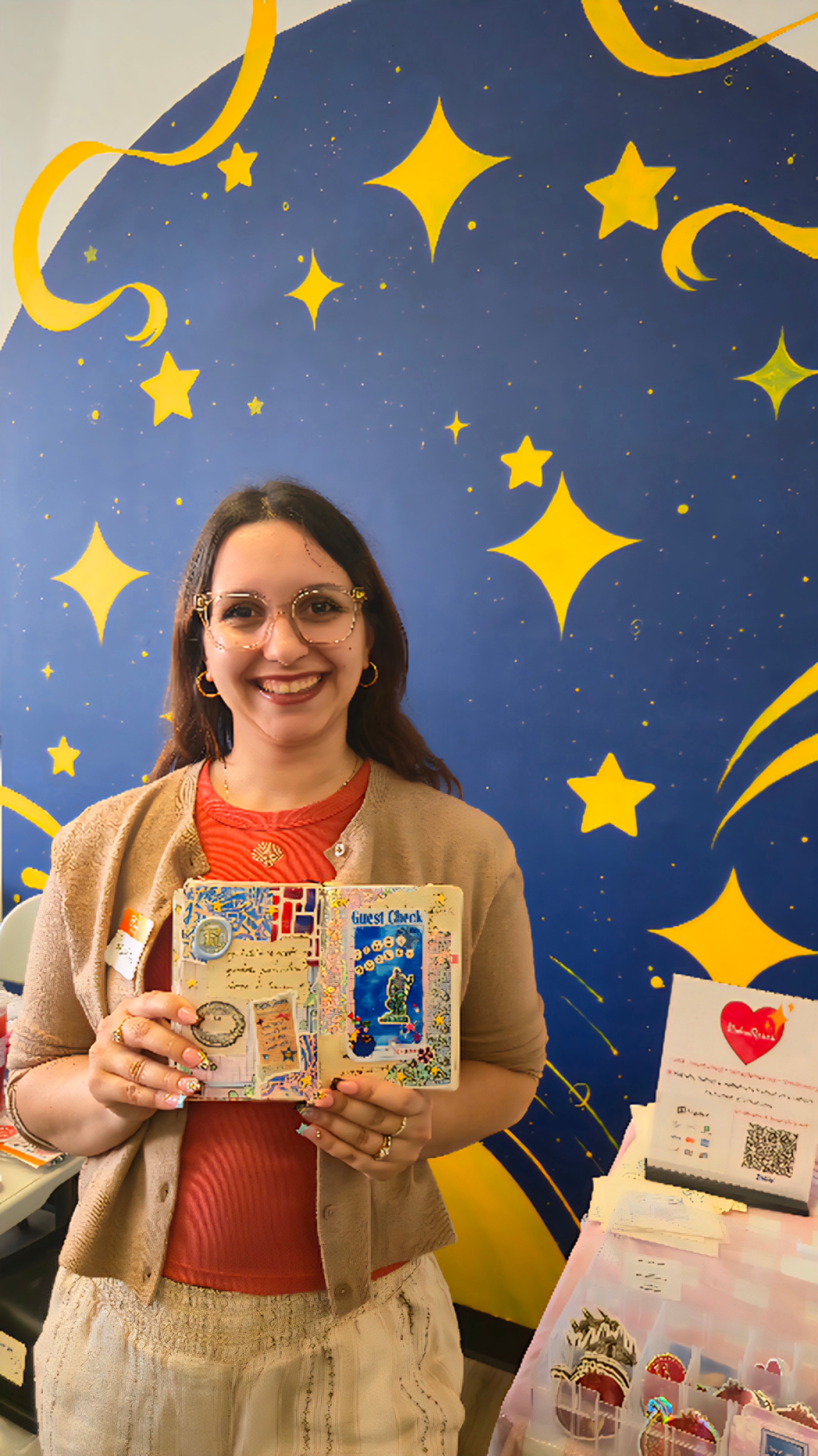 Rebeka standing in front of a blue mural holding her journal.