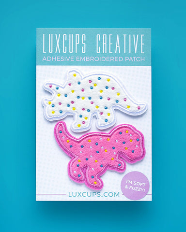 Embroidered patches that are designed to look like pink and white animal cookies, and shaped like dinosaurs