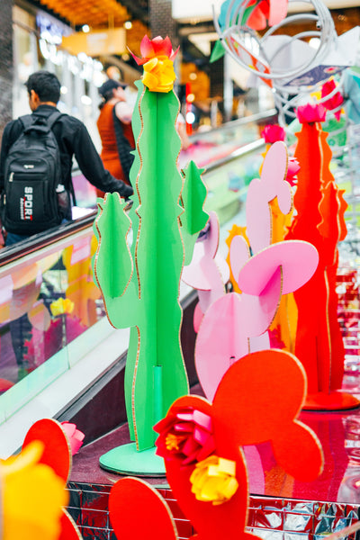 A procession of large multi-coloured cardboard cacti that are displayed between travellators at Broadway Shopping Centre
