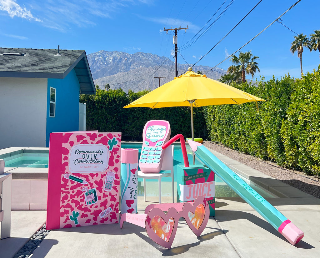 Colourful oversized cardboard props are arranged by a sunny pool