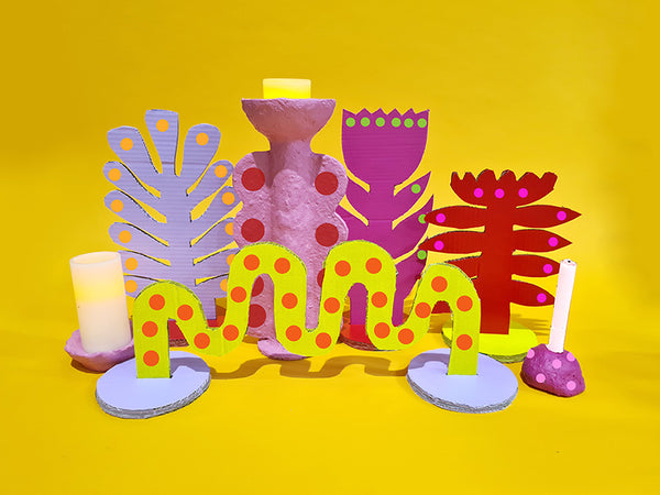 A collection of colourful handmade cardboard and papier mache table decor sits on a yellow backdrop.