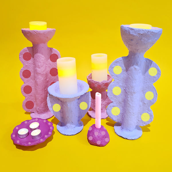 A collection of colourful papier-mâche candle holders sit on a yellow background