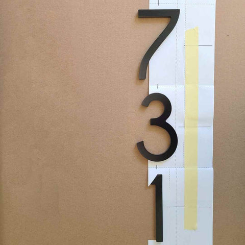 Vertical house number template prepared for address numbers fastened with adhesive.