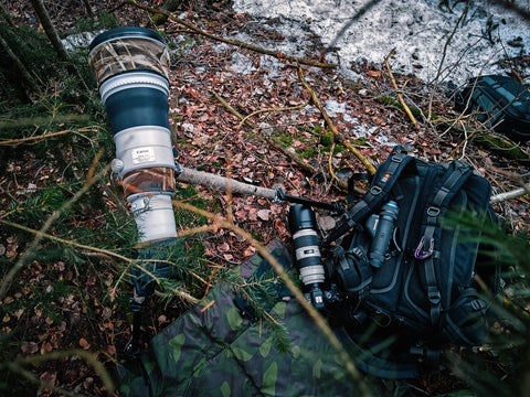 Kuvassa luontokuvaajan järjestelmäkamera ja Pulsar lämpökamera metsässä repun vieressä