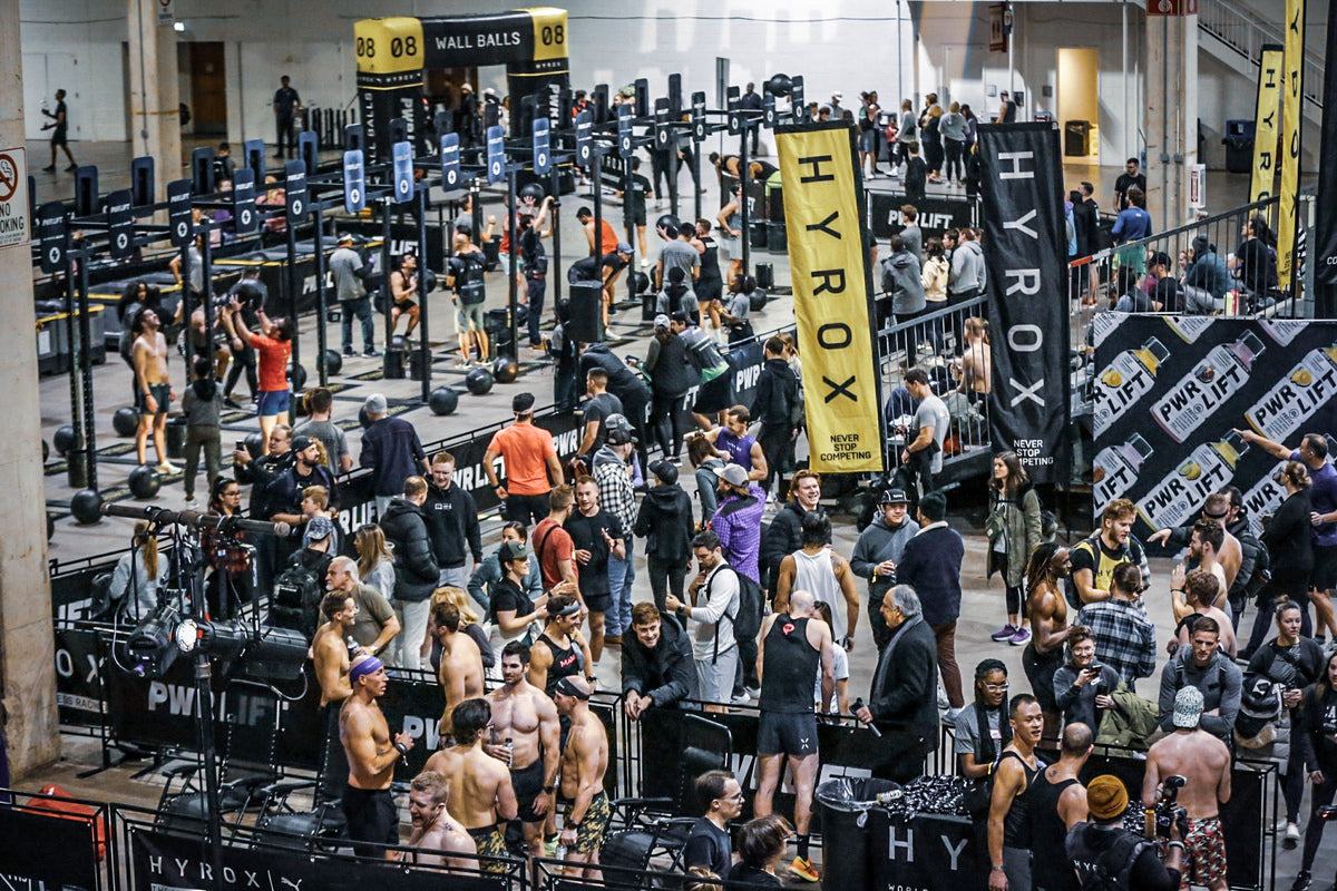 top HYROX athletes from across the world  warming up and talking in a large indoor gym 