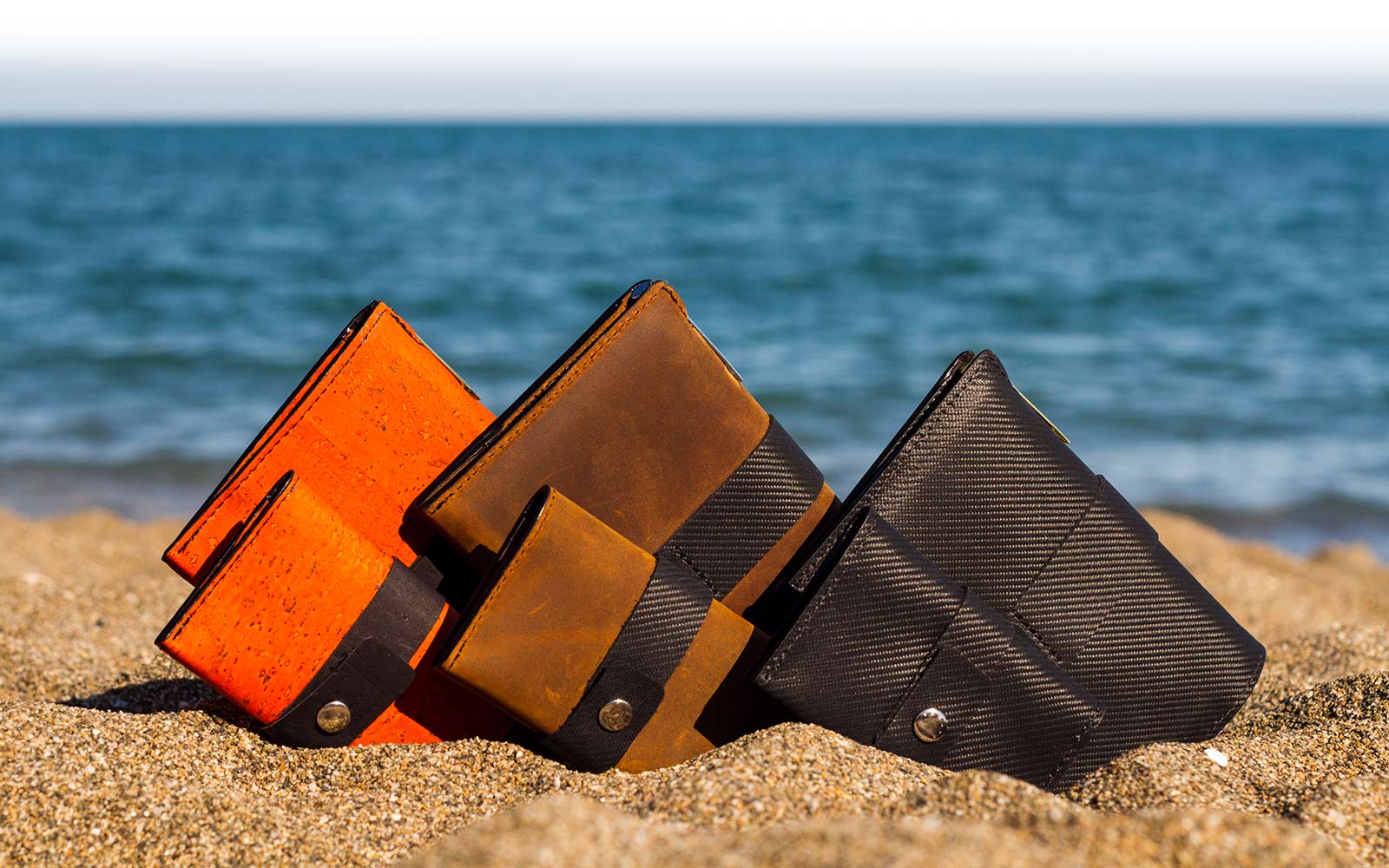 Traveller and Tasca wallets, black, brown and orange, on beach