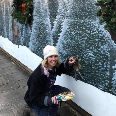 A picture of artist emma taylor painting a christmas themed mural with artist palette and brush in hand