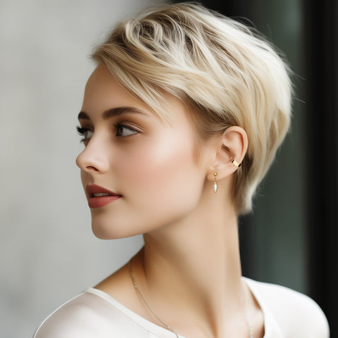Woman with short blond hair elegantly wearing a combination of pearl stud earrings and a wave-shaped ear cuff, creating a chic and stylish look