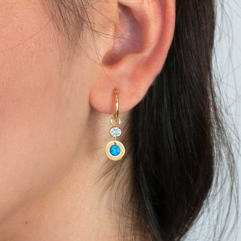 Hoop earrings featuring a dangling blue opal charm and cubic zirconia (CZ) on a woman's ear