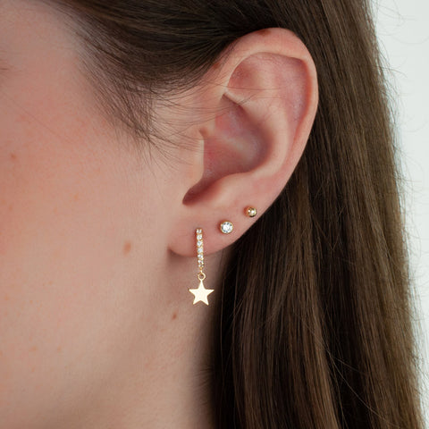 A woman wears a three gold earrings. CZ stud earring, hoop earring with star charm, ball stud earring