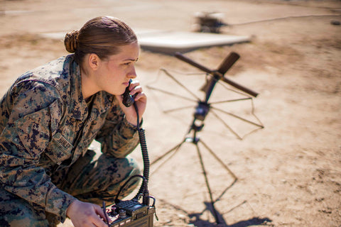 Female army soldier listening on a radio by an antenna