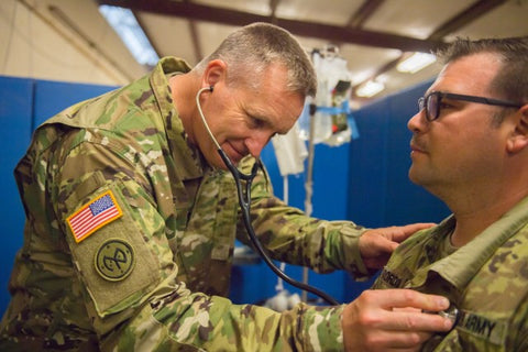 Doctor in camo uniform checking US Army soldier's heart with stethoscope