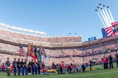 Military band playing in crowded stadium with jets flying overhead