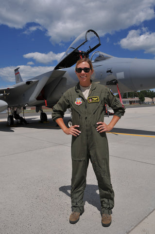 Female pilot in flight suit in front of jet.