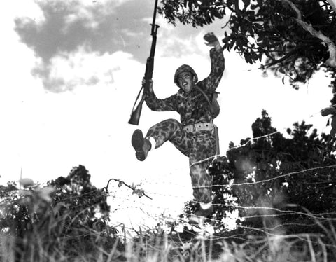 Black and white picture of soldier jumping over barbed wire