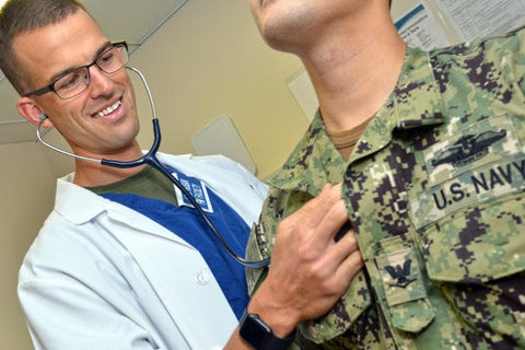 Doctor in white lab coat checking US Navy sailor's heart with stethoscope