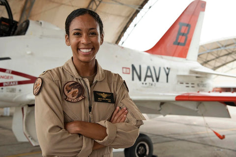 Female pilot in hanger standing in front of jet.