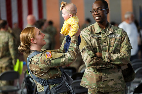 military dad and mom in camouflage uniforms holding infant