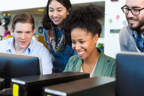 four people looking at computer screen smiling