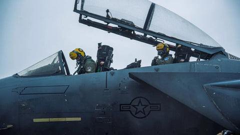 Pilots in fighter jet with canopy open.
