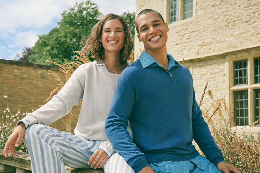 Woman and man sat on a wall in matching pyjamas and cashmere sweaters.