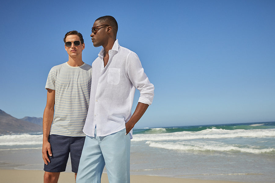 Two men on a beach one wearing a white linen shirt and the other in a striped t-shirt.