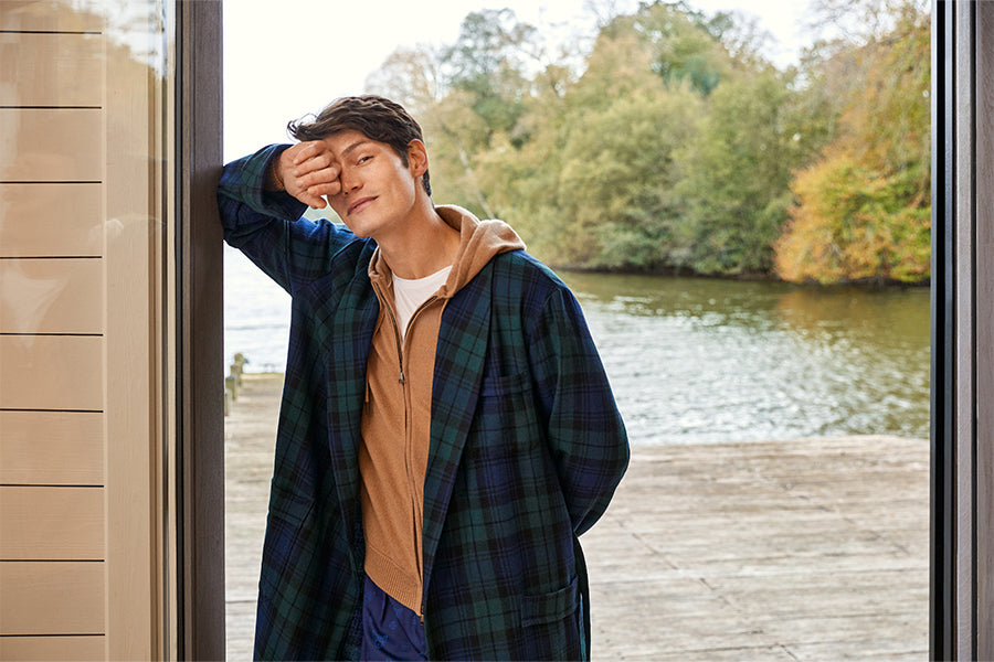 Man in wool gown leaning on door by a lake