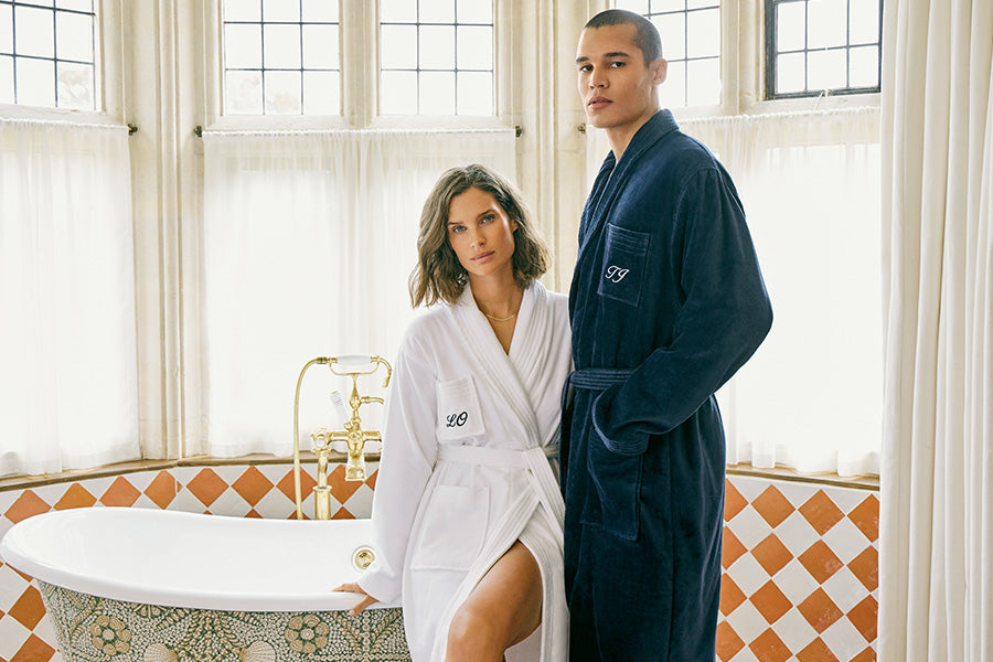 Man and woman by a bath in monogrammed dressing gowns