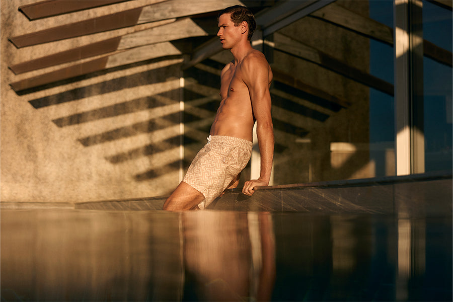 A man in swim shorts pulling himself out of a pool.