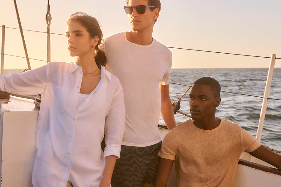 Two men and a woman on a yacht in linen tops and swim shorts.