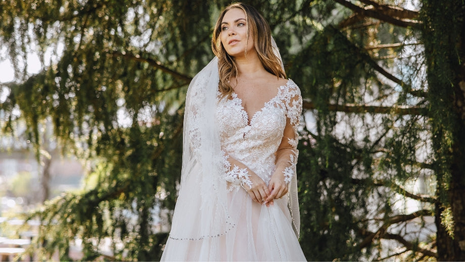 Image of bride wearing a long sleeve white lace wedding dress standing in front of a tree.