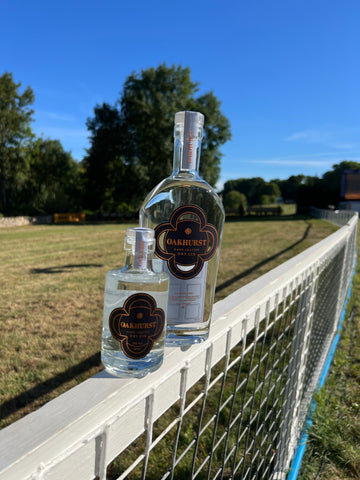 70cl and 20cl bottle of Oakhurst Gin sat on a fence around a horse cross country track.